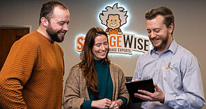 How StorageWise Self-Storage Experts Support Students, Families, and Local Businesses in Limerick 1 Three people smile and look at a tablet together in an office with a Storage Wise sign and cartoon mascot on the wall behind them.