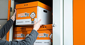 How StorageWise Self-Storage Experts Support Students, Families, and Local Businesses in Limerick 2 A person places an orange and white StorageWise box with a cartoon scientist logo into a storage unit, with more identical boxes stacked inside.