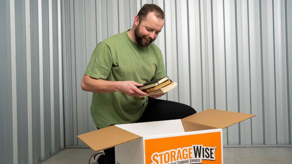 A smiling man in a green shirt packs books into a Storage Wise box inside a metallic-walled storage unit, showcasing convenient student storage in Ireland.