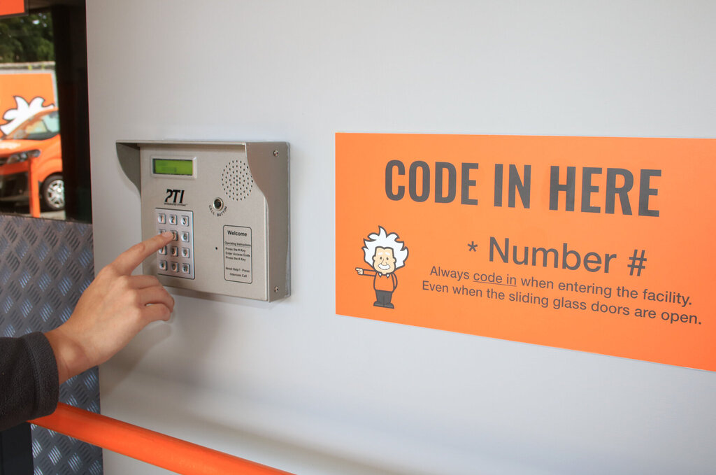 A person’s hand enters a code on a keypad next to an orange sign that says CODE IN HERE * Number #, reminding those with serviced office spaces to always code in when entering the facility.