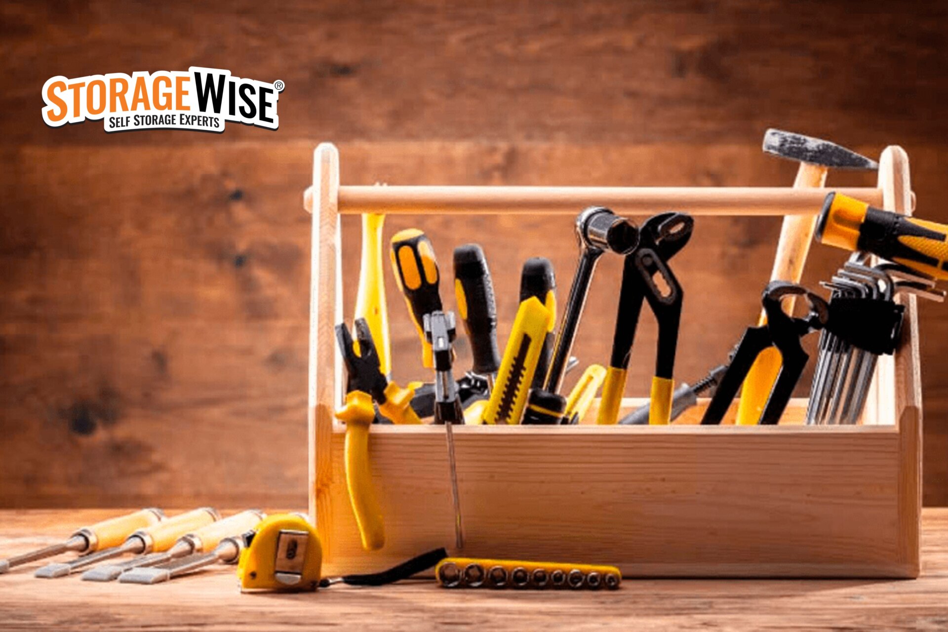 A wooden toolbox filled with various yellow and black hand tools sits on a wooden surface, offering the perfect business storage solution for tradespeople storage or tool storage needs. The Storage Wise logo appears in the top left corner of the image.