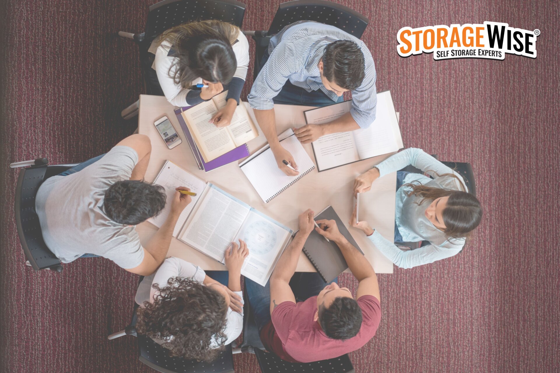 Six people sit round a table studying with notebooks, pens, and textbooks. The STORAGE WISE logo is in the top right corner. The scene has a collaborative, academic atmosphere&mdash;perfect for students planning to store your belongings or looking for reliable storage for students whilst studying abroad.