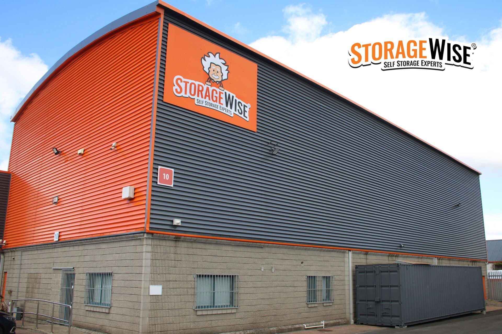 A modern storage facility with grey and orange cladding, a large Storage Wise sign, and a shipping container outside&mdash;perfect for those renting office space in Limerick or seeking their first business office. The company logo and slogan are also visible on the building and in the top right corner.